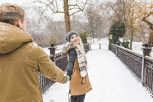 Portrait of happy teenage girl standing hand in hand with her boyfriend on footbridge on a snowy day