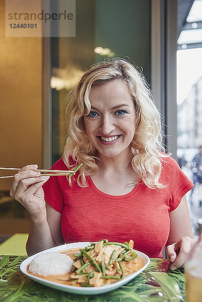 Portrait of smiling blond woman eating vegetarian Asian dish