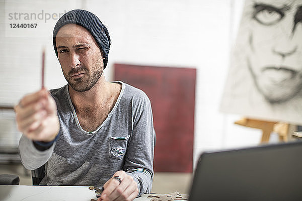 Artist sitting at his desk in studio checking pencil