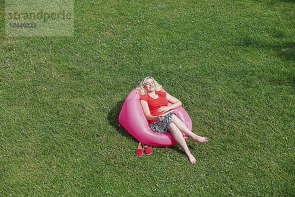Happy pregnant woman sitting in inflatable seat on meadow