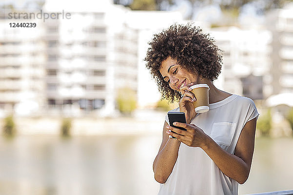 Young woman taking a break outdoors  holding cup of coffee and smartphone