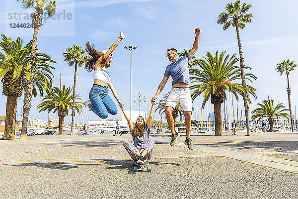 Carefree friends having fun with a skateboard on a promenade with palms