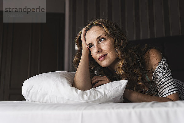 Thoughtful woman lying on bed at home looking away