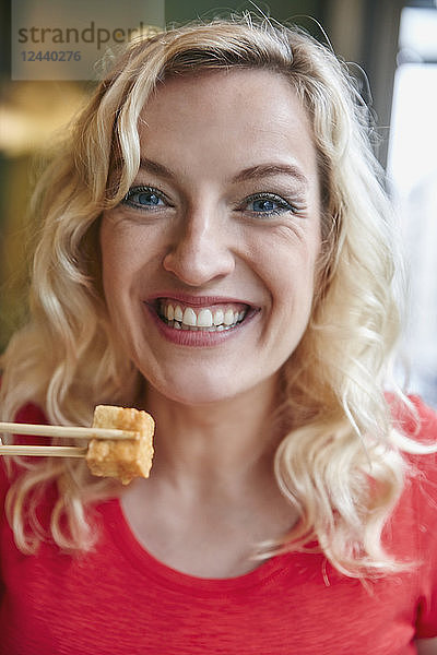 Portrait of happy blond woman eating tofu