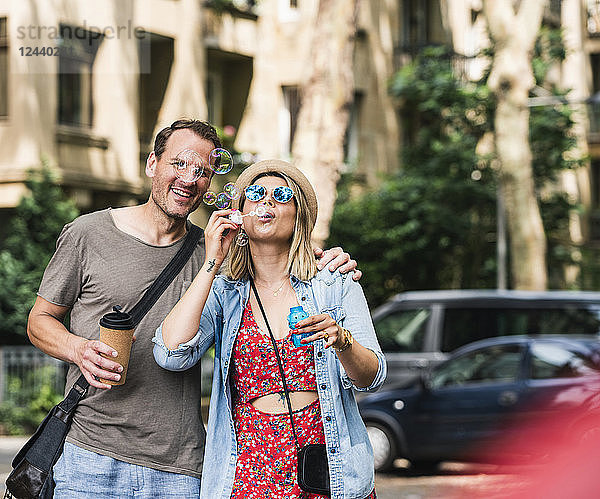 Happy couple with coffee to go blowing soap bubbles in the city