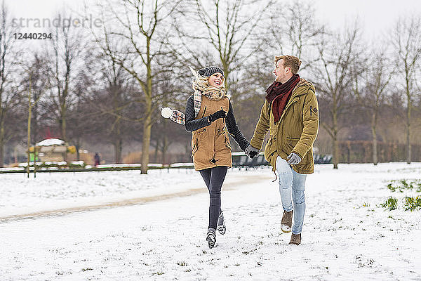Happy young couple in love walking hand in hand in a park on snowy day