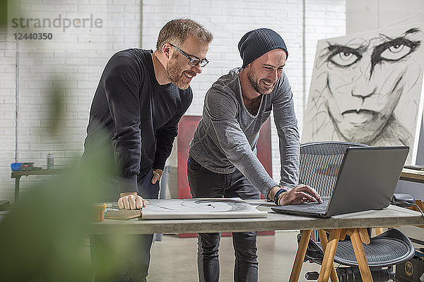 Smiling artist using laptop with man in studio