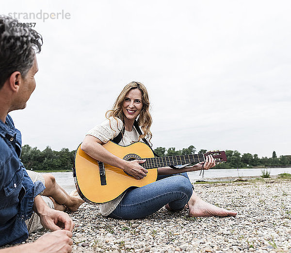 Happy woman with man at the riverside playing guitar