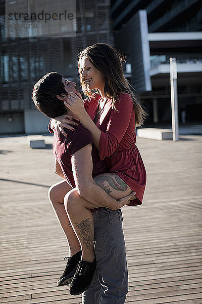 Young man lifting up happy girlfriend on city square