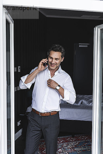 Smiling businessman on cell phone in bedroom at home getting dressed