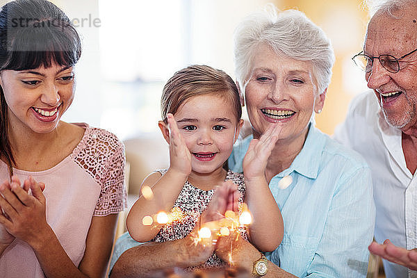 Little girl lwatching sparklers on a birthday cake  sitting on grandmother's lap