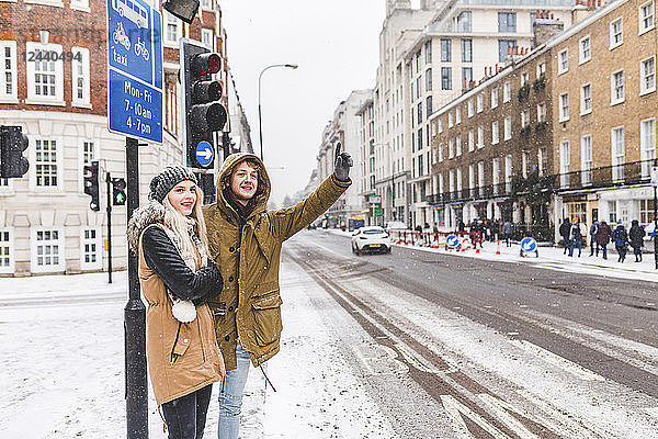 UK  London  young couple standing at roadside hailing taxi in winter