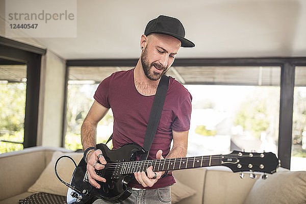 Young man playing electric guitar in living room at home