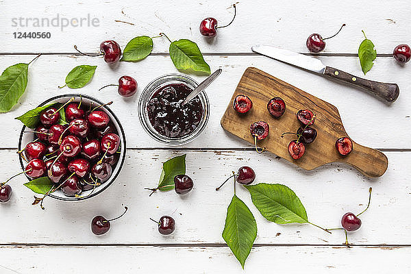 Jar of cherry jam and cherries on white wood