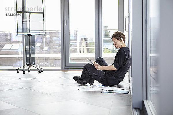 Businesswoman sitting on the floor in office using tablet