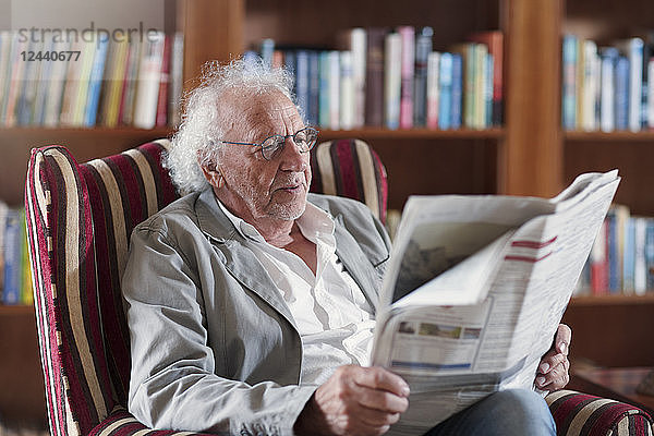 Senior man sitting in library  reading newpaper