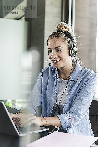Young businesswoman sitting at desk  making a call  using headset and laptop