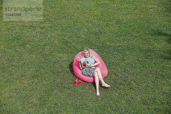 Woman sitting in inflatable seat on meadow looking at photo book