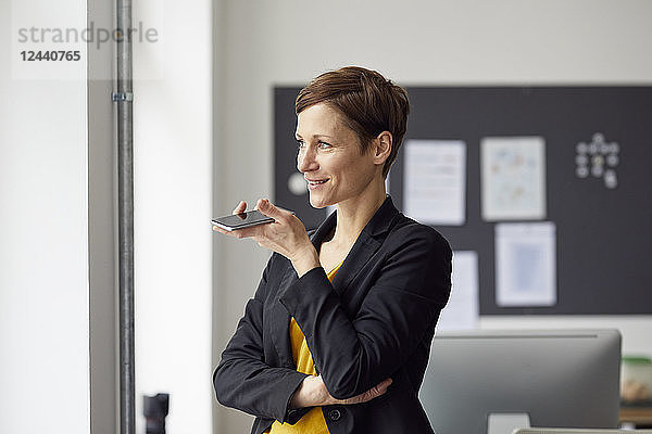 Attractive businesswoman standing in office  using smartphone