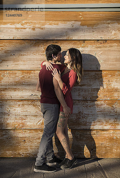 Affectionate young couple hugging at wooden wall