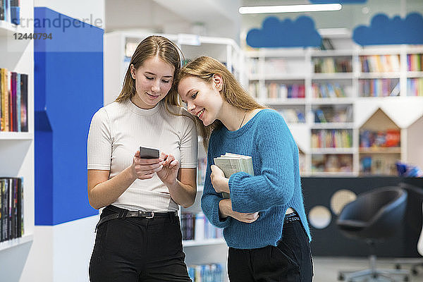 Two teenage girls in a public library looking at cell phone