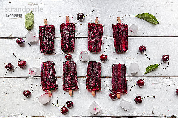 Homemade cherry ice lollies  ice cubes and cherries on white wood