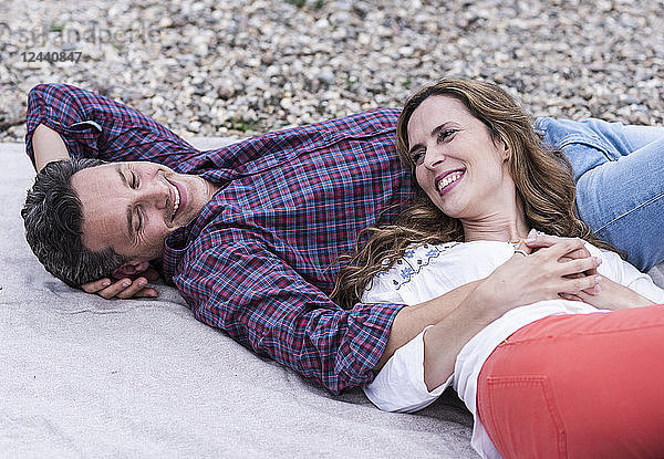 Happy affectionate couple lying on a blanket at pebble beach