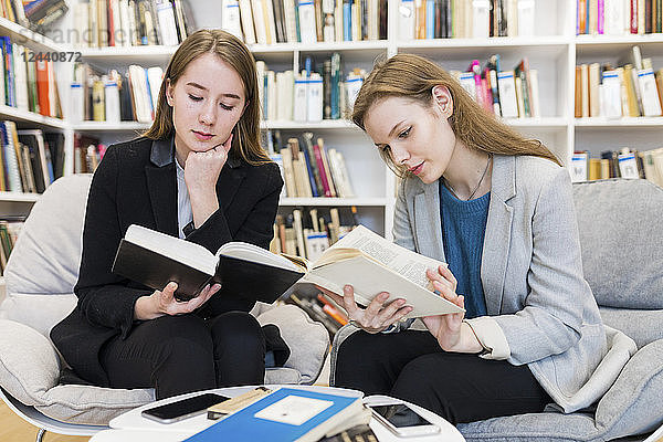 Two teenage girls sitting in a public library reading books