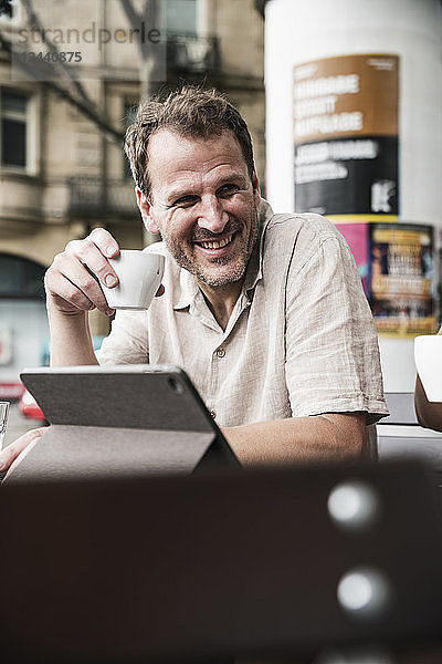 Smiling man with tablet and coffee at an outdoor cafe