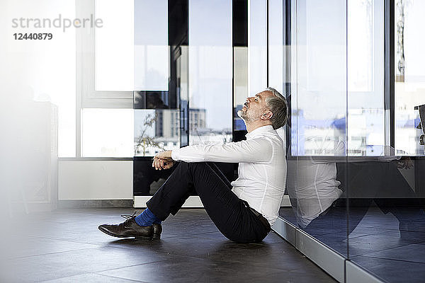 Businessman sitting on the floor in office with closed eyes