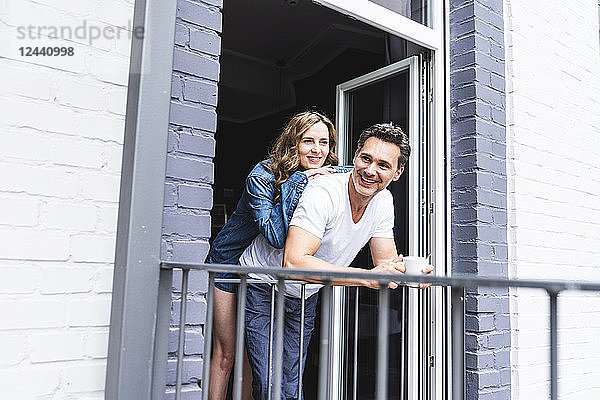 Happy couple in nightwear at home at balcony door