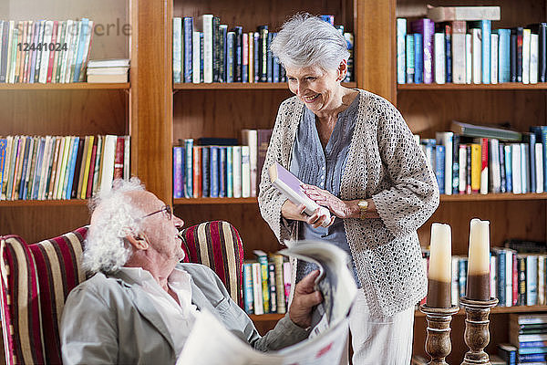 Senior man and woman sitting in library  reading book and newspaper