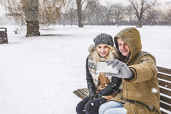 Happy young couple taking selfie with cell phone on snowy day in the park