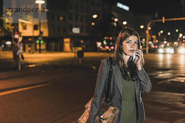 Portrait of young businesswoman with leather bag on the phone at night