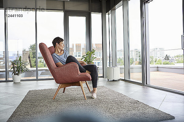 Woman sitting in armchair at home looking out of balcony door
