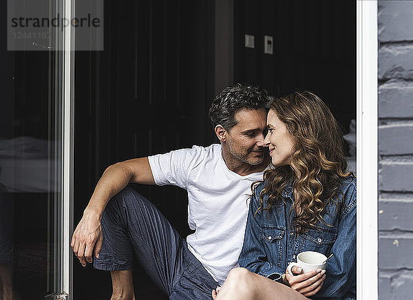 Affectionate couple in nightwear at home sitting at French window