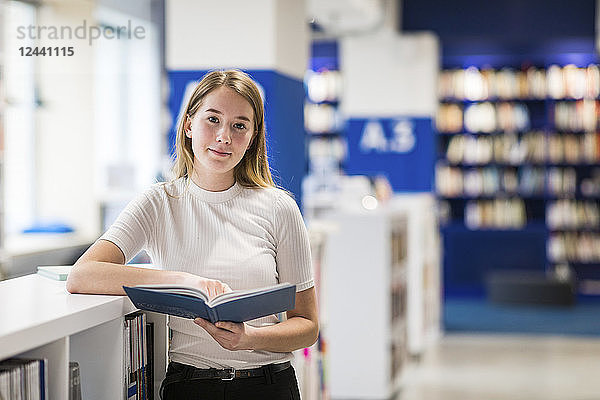 Portsrit of relaxed teenage girl with book in a public library