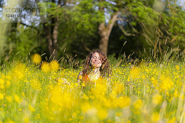 Young woman with closed eyes sitting on flower meadow