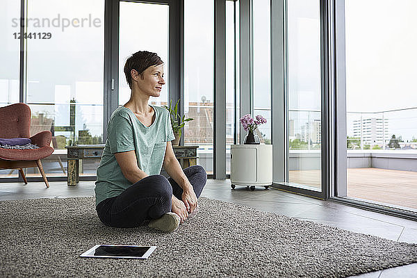 Woman sitting on the floor at home with tablet looking out of balcony door