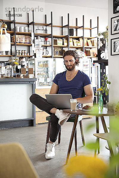 Portrait of young man sitting in a coffee shop using laptop