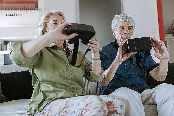 Senior couple at home sitting on couch holding VR glasses