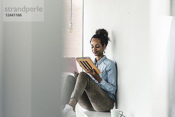 Young businesswoman sitting on shelf  using digital tablet