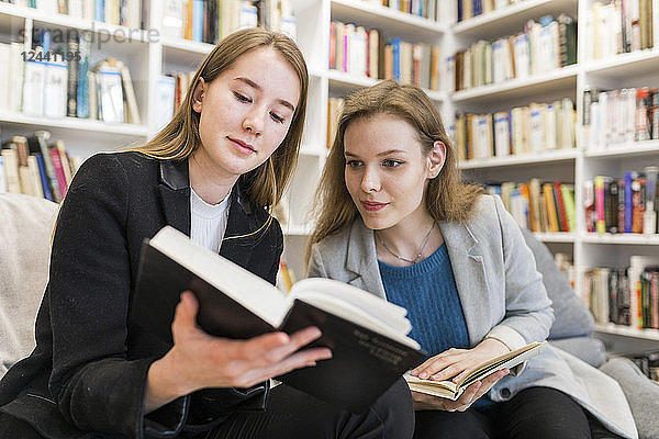 Portrait of two teenage girls sitting in a public library looking at a book