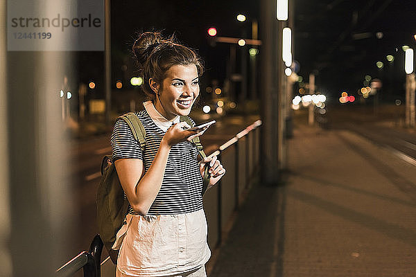 Portrait of young woman on the phone waiting at station by night