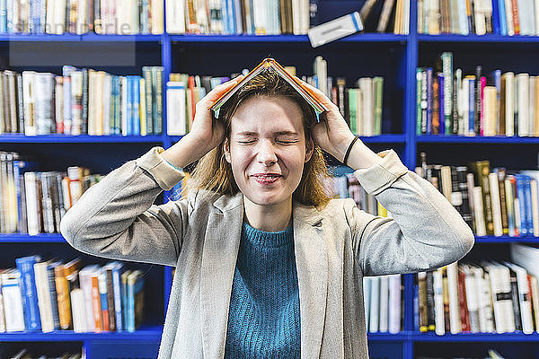 Portrait of teenage girl with book on her head in a public library