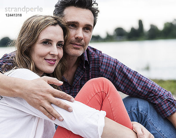 Affectionate happy couple sitting at the riverside