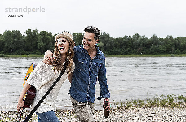 Happy couple walking at the riverside with beer bottle and guitar