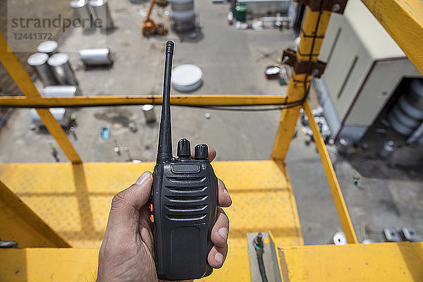 Hand holding walkie talkie on top of a crane on construction site