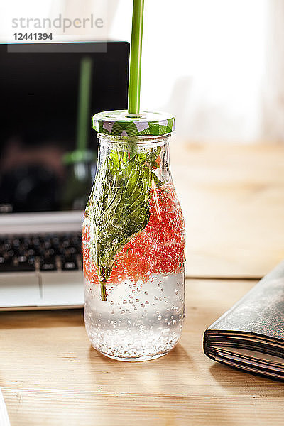 Glass bottle of detox water infused with red grapefruit and mint on desk