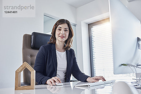 Portrait of smiling young businesswoman at desk in office with architectural model